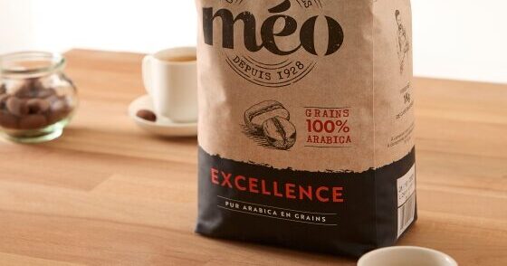 un sac de grains de café meo est posé sur un comptoir de cuisine en bois, à côté de deux petites tasses de café et d'un pot de noix.