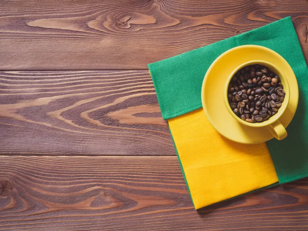 Vue plongée sur tasse jaune remplie de grain de café avec serviette aux couleurs du brésil