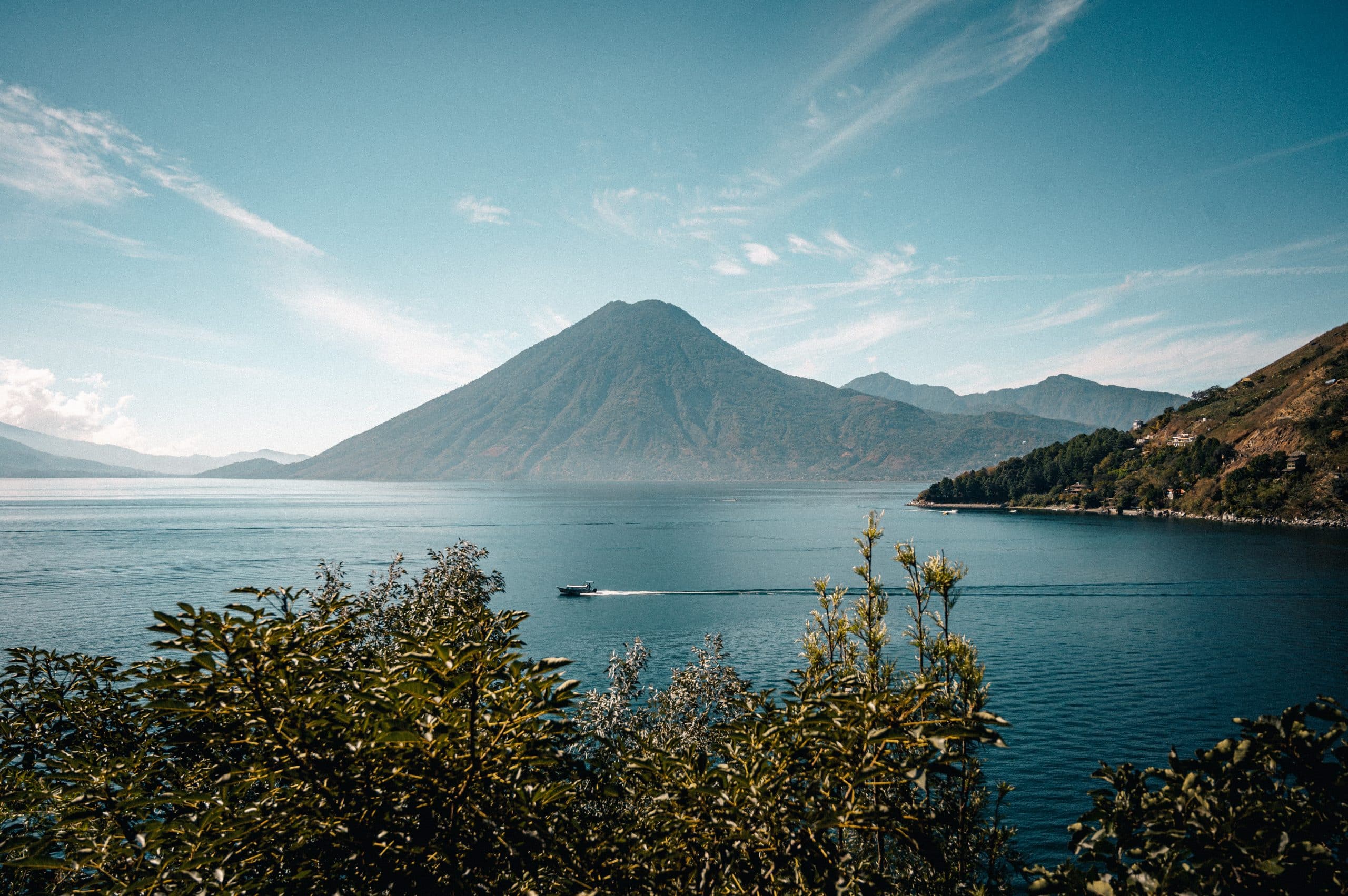 scenic view of a boat sailing in lake atitlan against a mountain covered with greenery in guatemala