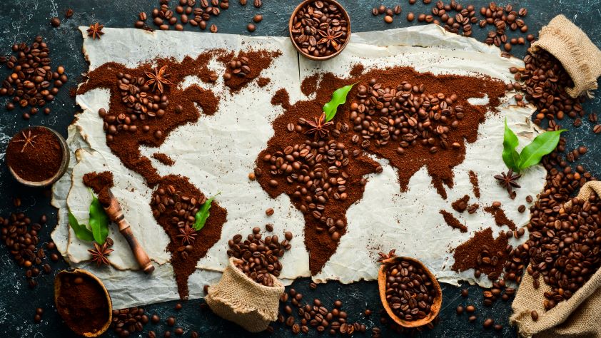 une carte du monde entourée de marc de café, entourée de grains de café, d'anis étoilé et de feuilles vertes fraîches, posée sur une surface semblable à du parchemin froissé.