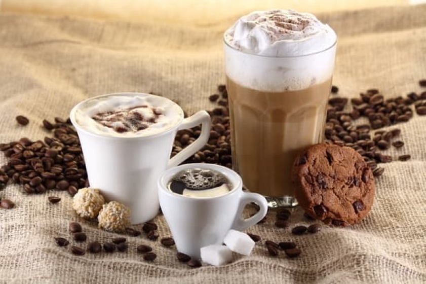 trois boissons au café et un biscuit aux pépites de chocolat, entourés de grains de café.