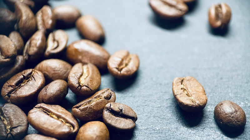 vue rapprochée de grains de café torréfiés dispersés sur une surface sombre.