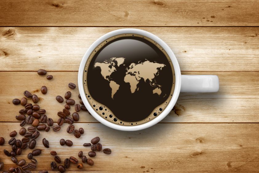 une tasse de café sur une table en bois, la surface du café ressemblant à une carte du monde. les grains de café sont dispersés sur la gauche.