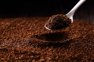 une cuillère en métal tient un petit monticule de café moulu au dessus d'un tas plus gros. le café est brun foncé et finement texturé sur un fond noir.