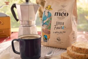 un sac de café méo est posé à côté d'une tasse, d'une machine à expresso, de tranches de pain et de beurre sur une table de petit déjeuner, vous invitant à commencer votre journée avec le riche arôme du café.