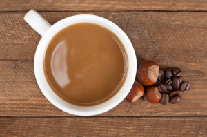 une tasse de café au lait sur une surface en bois, à côté de noisettes entières et de grains de café.