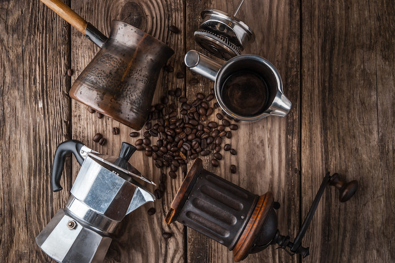 quatre cafetières différentes et des grains de café éparpillés sur une surface en bois rustique.
