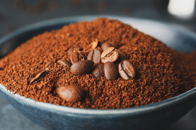 gros plan sur des grains de café entiers reposant sur un monticule de café moulu dans un bol sombre.