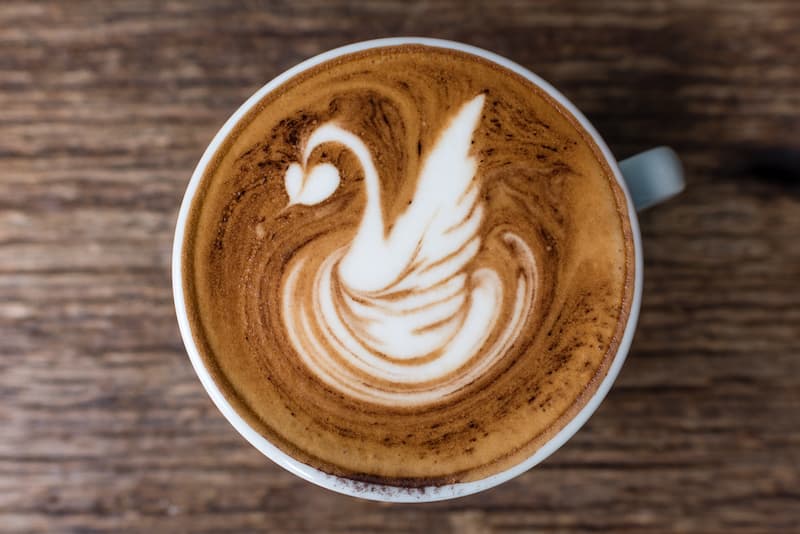 une tasse de café avec un art latté en forme de cygne, vue d'en haut, sur une surface en bois.