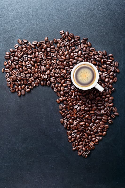 une tasse de café est posée sur une pile de grains de café en forme de continent africain, placée sur une surface sombre.