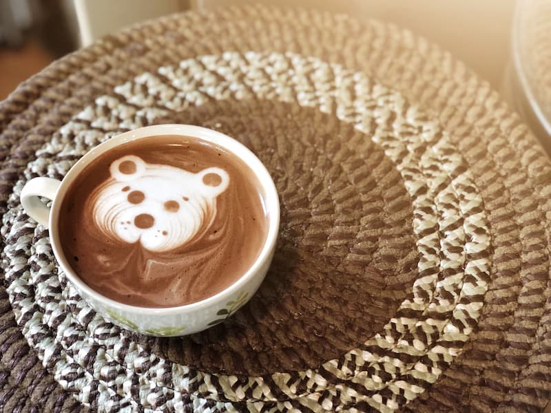 une tasse de café avec une mousse ressemblant à un visage d'ours est posée sur un napperon circulaire tissé.